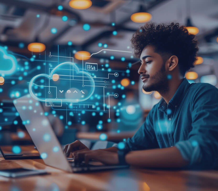 A focused young man engages with cloud technology graphics on a laptop at a modern workspace.