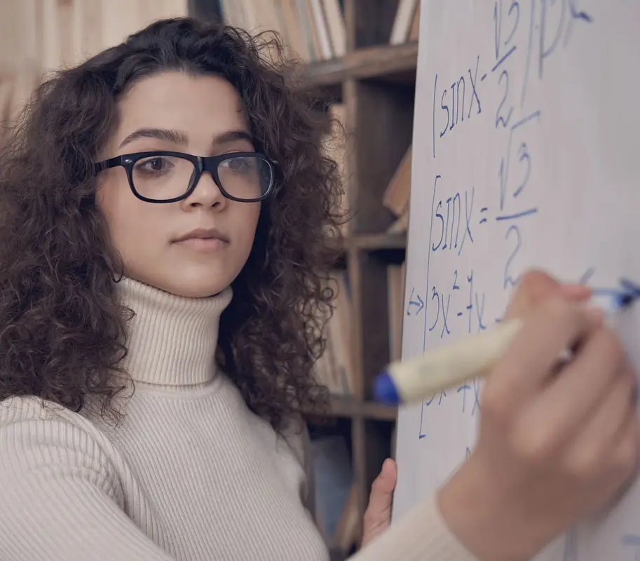 Young latin math school teacher wearing glasses writing on whiteboard. Pharmacy Technician